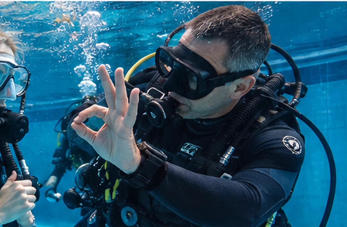 Tauchlehrer erklärt einer Taucherin unter Wasser ein Handzeichen